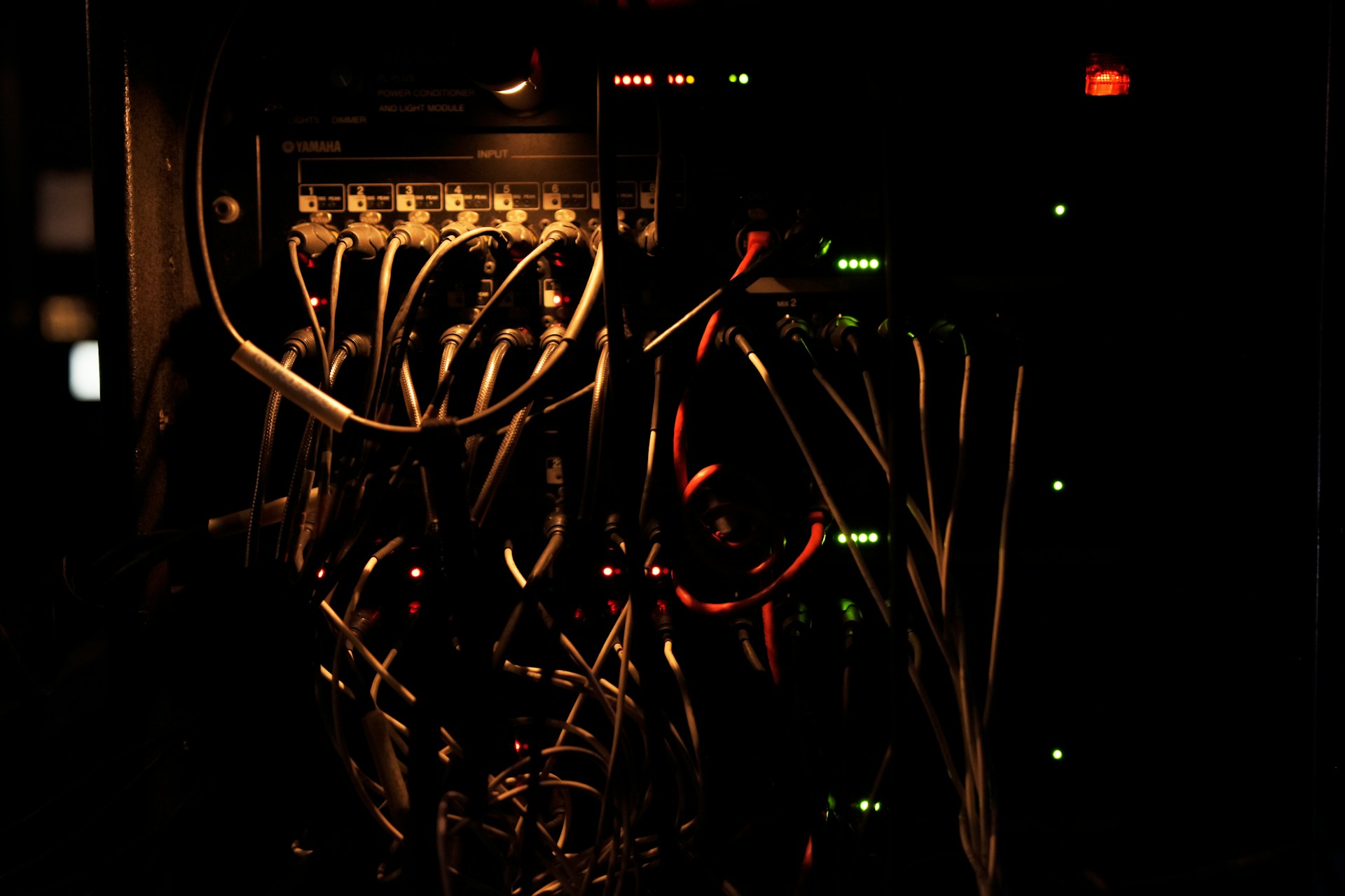 Dimly lit equipment rack filled with tangled cables and small red-and-green indicator lights.