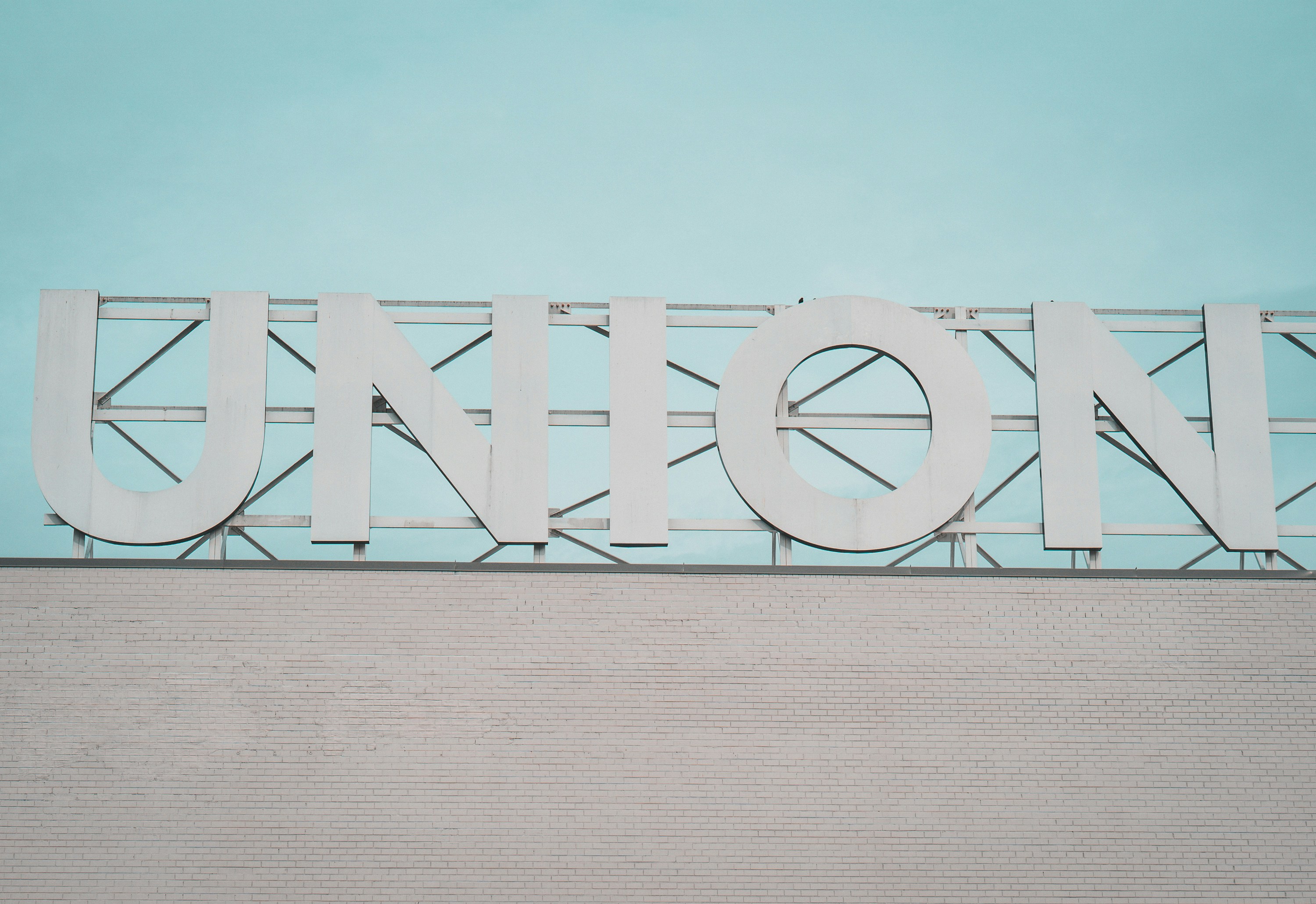 Photo of a large, white sign with the letters &#39;UNION&#39; against a light blue sky, mounted on top of a white brick building.